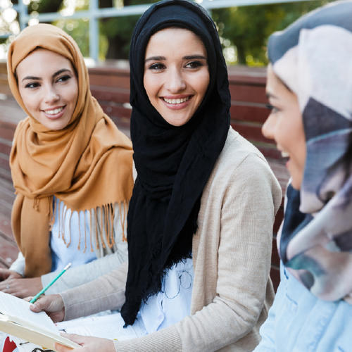 Four older adults sitting outdoors together, laughing and enjoying a relaxed moment in a natural setting while wearing casual clothes.